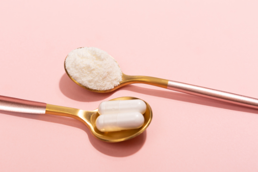 two spoons on a pink background - one with powdered collagen, one with pill-form collagen